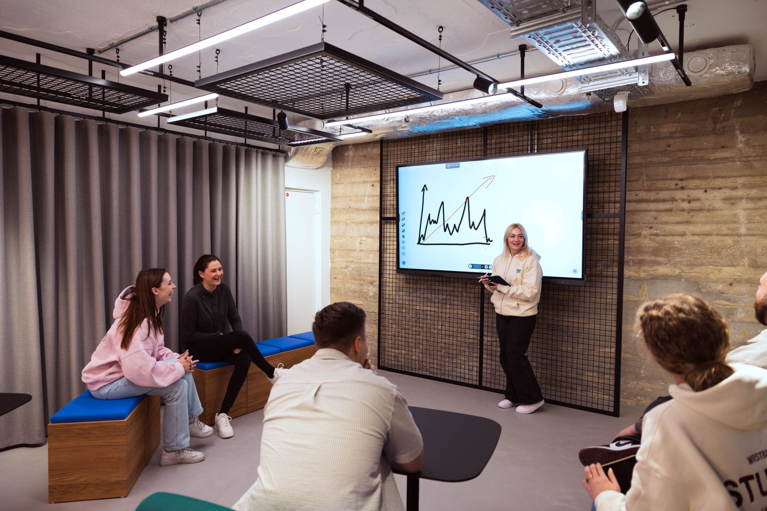 F44FBCD3-4985-4B37-A17C-5D79D659851C Auf dem Bild sieht man einen Vortrag vor einem Whiteboard. Alle Personen auf dem Bild lachen untereinander.